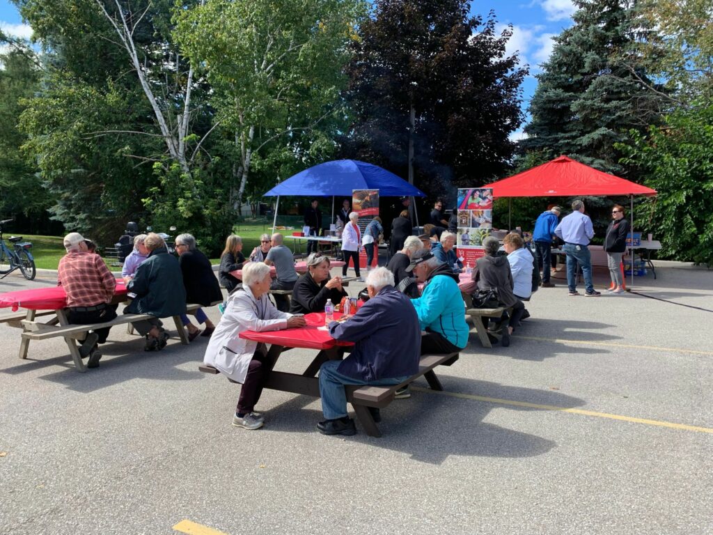 Community members enjoying BBQ lunch at picnic tables.
